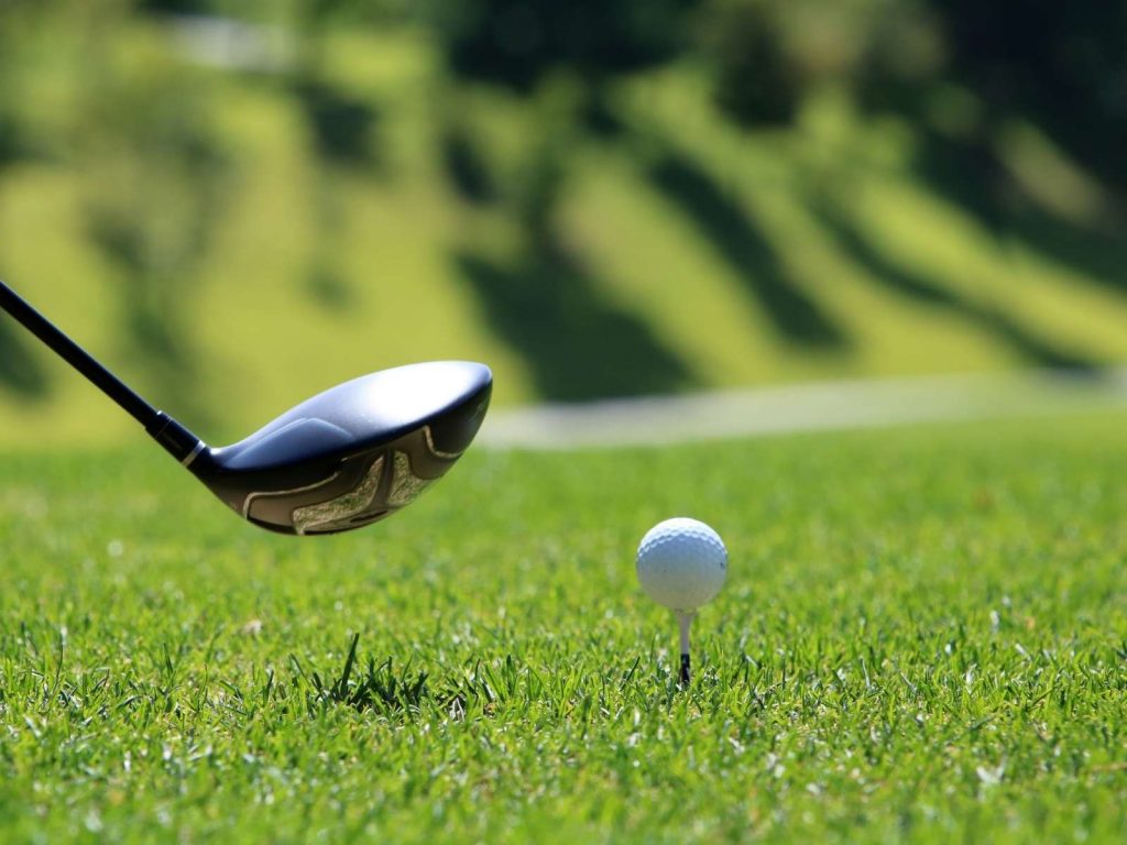 golf ball on a gold tee with a club by it